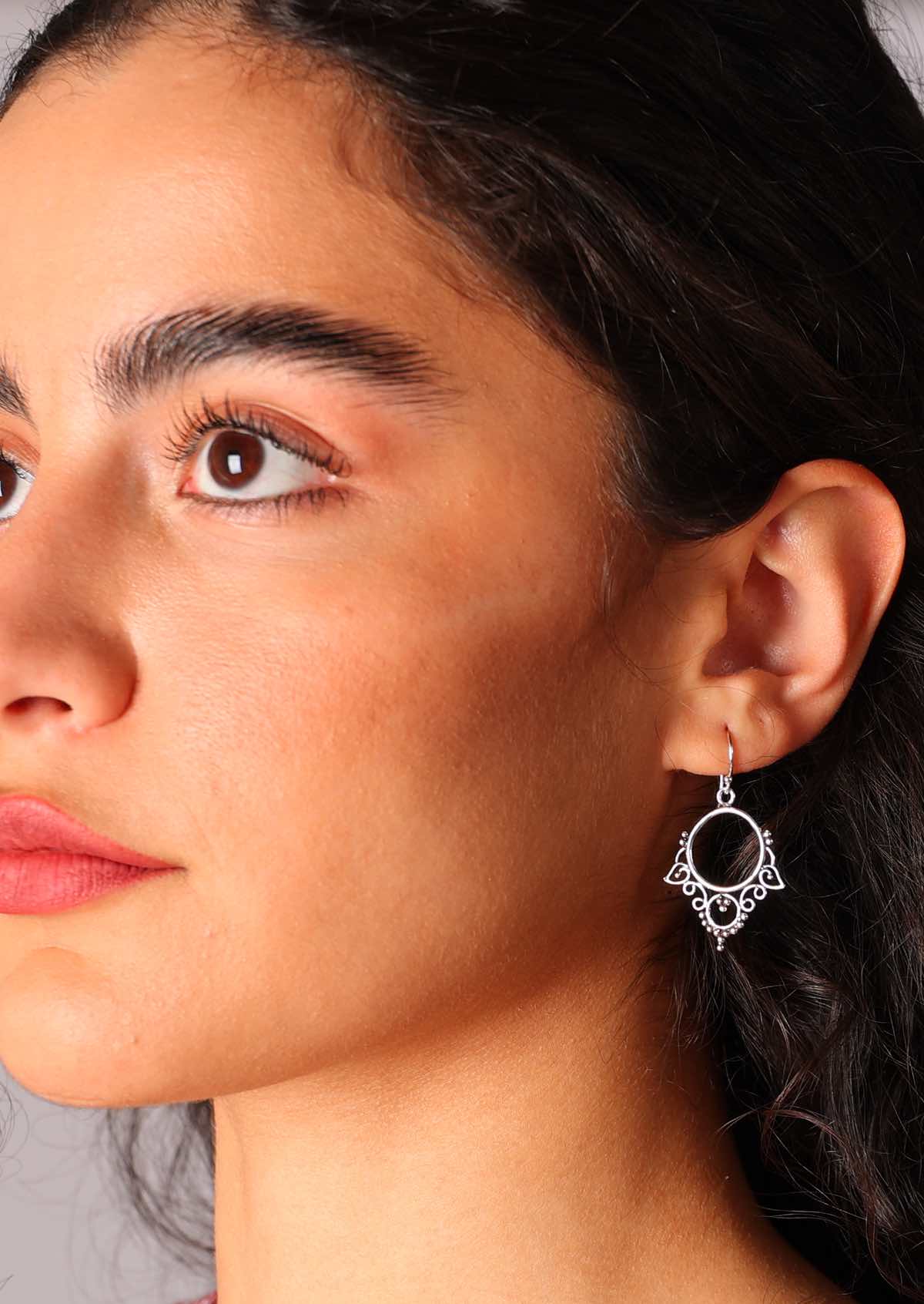 Sterling silver earrings feature a delicate hoop suspended from a wire hook, adorned with intricate detailing along the bottom half