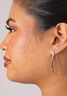 Woman wears silver sleek curved fixed hook earrings with subtle ridge in front