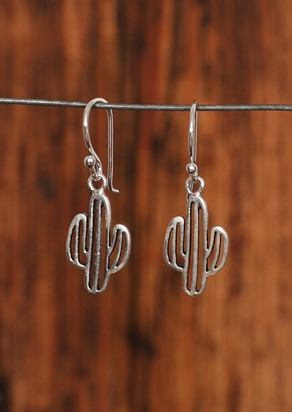 Sterling silver cutout cactus earrings suspended from wire hook.