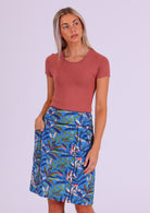 Model wears cotton A-line skirt in leafy print on a blue base with contrasting piping with her hand in pocket