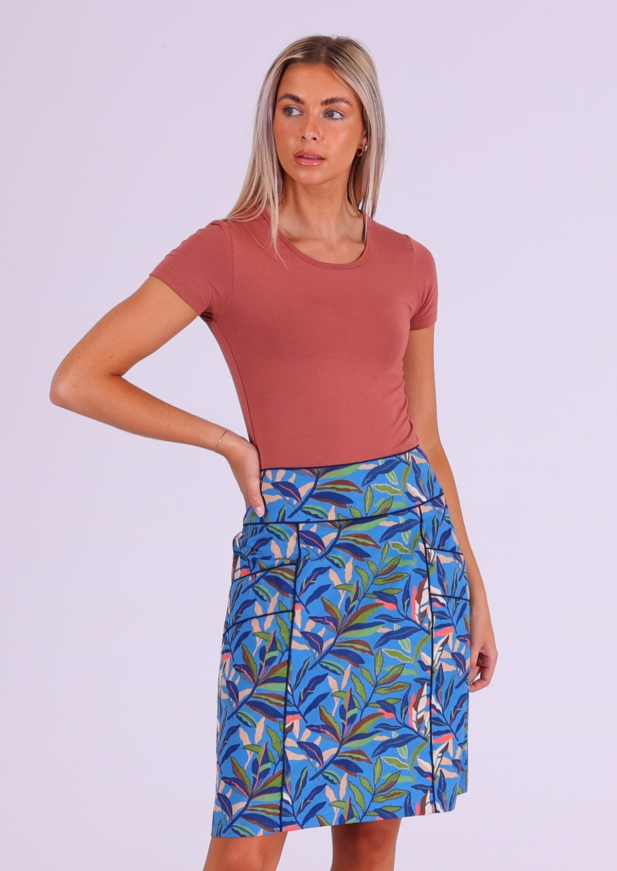 Woman stands in blue based multi-coloured leafy print cotton above knee skirt with pockets 