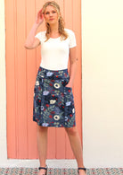 Model wears cotton above knee length skirt in beautiful blue floral print with pops of red with hand in pocket