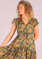 Closeup of model wearing green based floral rayon sundress with buttoned bodice and shoestring ties