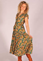 Model holding skirting of floral rayon sundress with shoestring ties and tulip sleeves