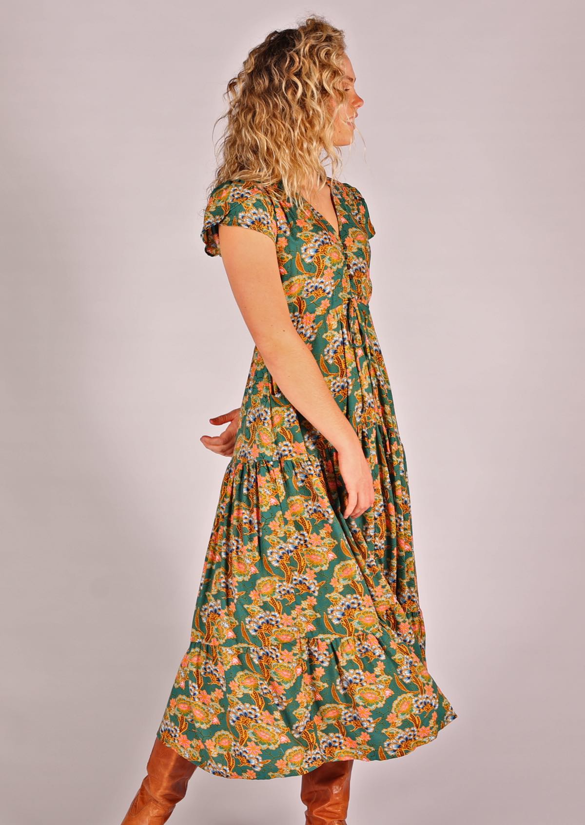 Model posing to the side wearing green based floral rayon sundress with buttoned bodice and tulip sleeves