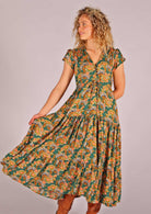 Model facing to the side and holding skirting of green based floral rayon sundress with full skirt