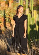 Woman wears black rayon maxi dress with  voluminous tiered skirt and buttoned bodice