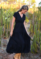 Woman stands in black rayon maxi dress with V-neckline and buttoned bodice and hidden side pockets