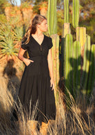 Woman poses in black rayon maxi dress with V-neckline, buttoned bodice, waist-tie and pockets