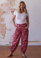 Model wears floral print on a red base cotton harem pants with buttoned ankle and pockets