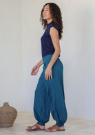 Side pose of model wearing 100% cotton wide leg pants in deep teal with pockets, cuffed ankles and shirred back waist 