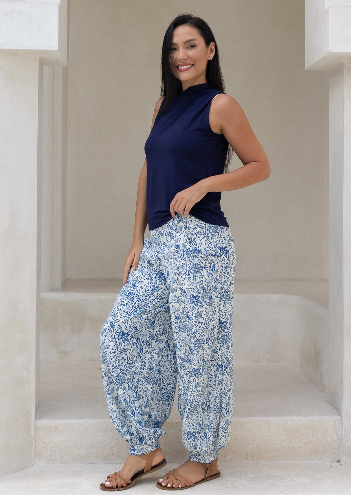 Woman wearing a navy sleeveless top and blue cotton floral harem pants standing in a neutral setting.