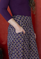 Close up of floral motif print on a purple base cotton pants, with model's hand in pocket