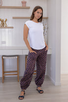 Woman wears cotton floral print harem pants with a wide waistband, with hands in pockets