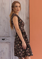 Model poses sideways wearing a mid length tailored crossover dress in beautiful black based floral print.