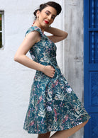 Side view of woman wearing the Alice Dress Verdure showing the flattering fit and floral print with hand in pocket