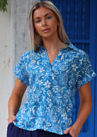 Woman wears cotton loose fit short sleeve top in blue floral print, with V-neck and collar