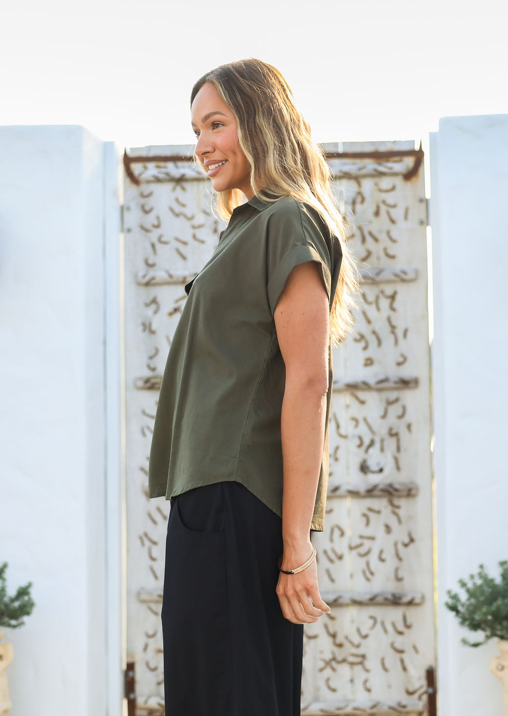 Woman stands in a side pose wearing a relaxed fit cotton collared top with short sleeves and V neckline