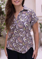 Model wears short sleeve relaxed fit cotton top with V-neckline and collar, in coral pink, lime green and beige florals on taupe base.
