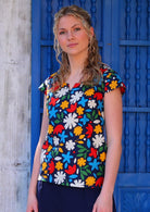 Woman poses in cap sleeved cotton tailored top in fun bold floral print on dark blue base