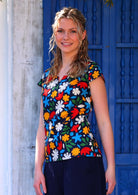 Woman stands turned to side in cotton cap sleeved top in fun bold print