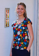 Model stands in bold floral print cotton top with pops of red, yellow, blue, white, olive green on a dark blue base