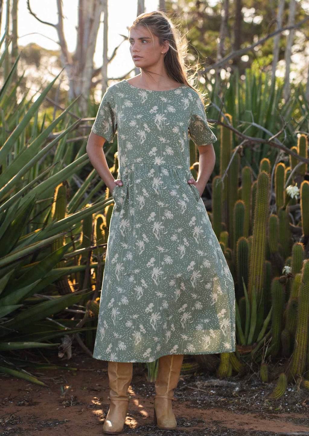 Woman wears midi length cotton dress with short sleeves and high round neckline with her hands in pockets