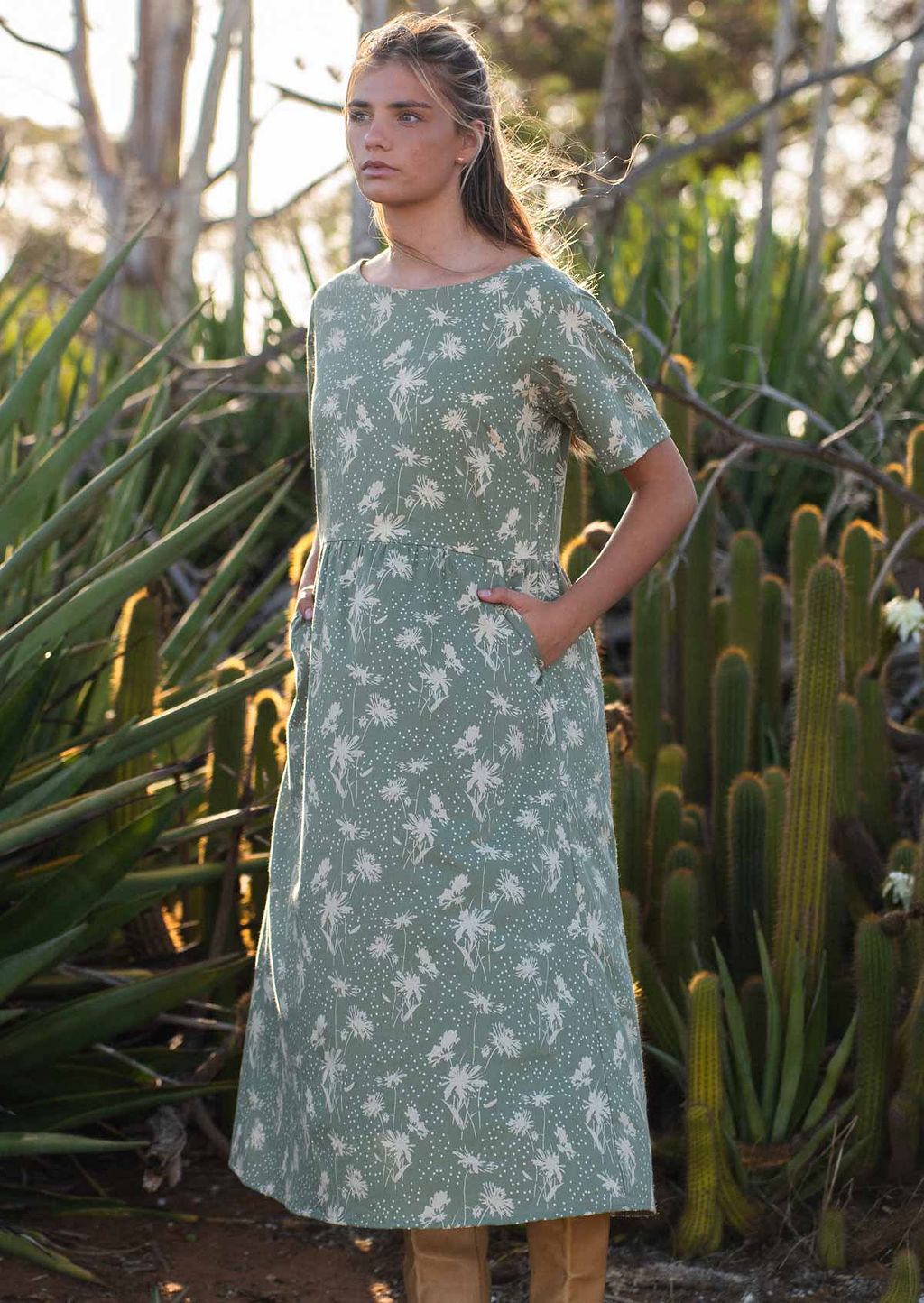 Model wears green based cotton midi length dress with T-shirt style sleeves and pockets