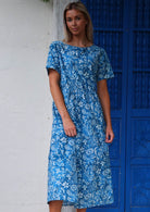 Model wears blue floral cotton midi length dress with wide round neckline and short sleeves