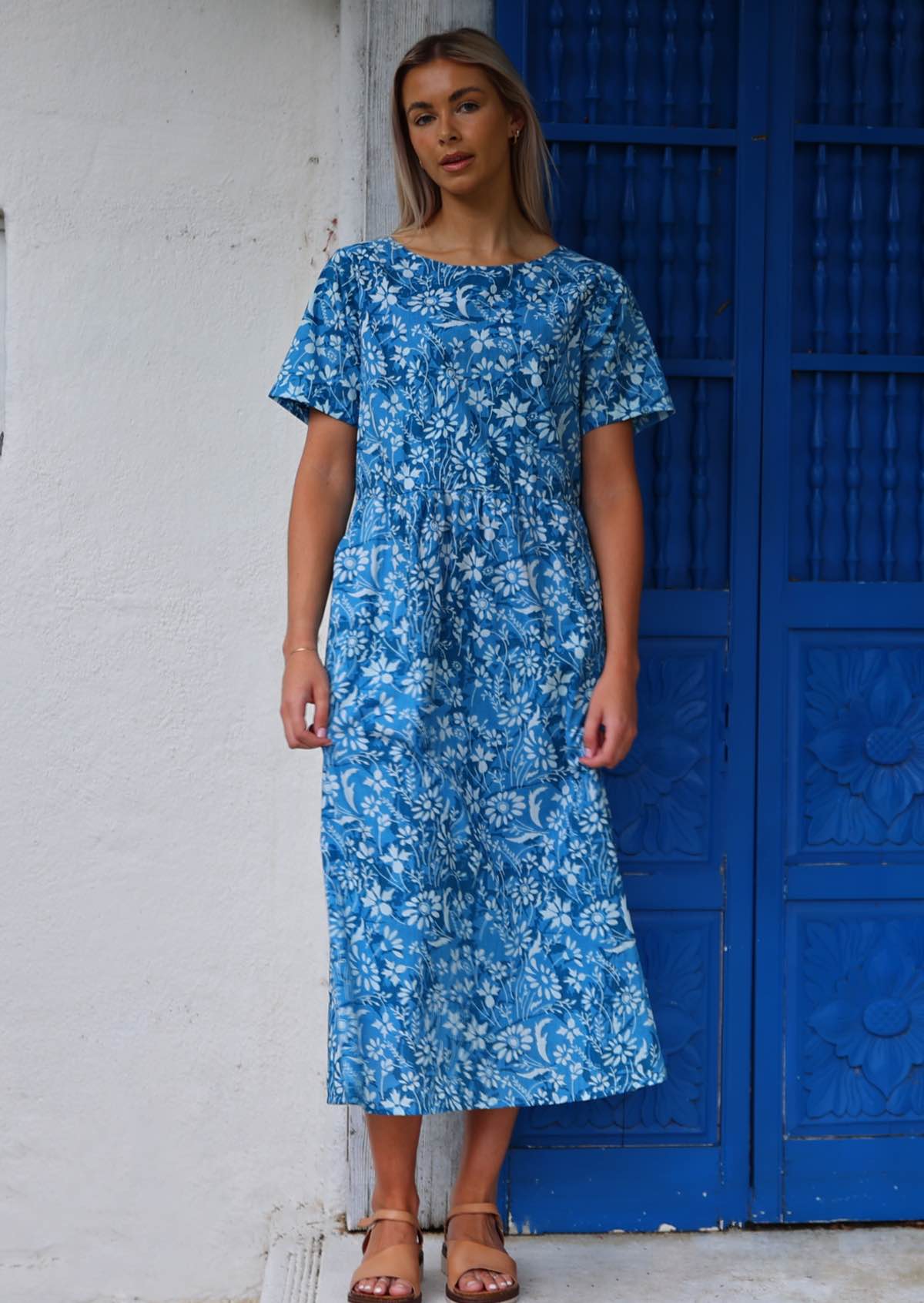 Model stands in 100% cotton blue floral print midi length dress with short sleeves