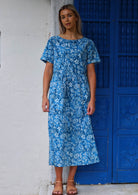 Model stands in 100% cotton blue floral print midi length dress with short sleeves