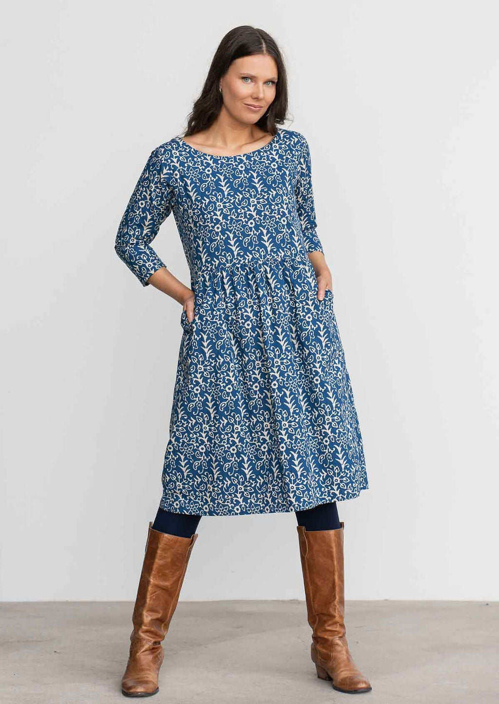 Woman in blue cotton, floral, knee length sundress with sleeves,  with hands in pockets