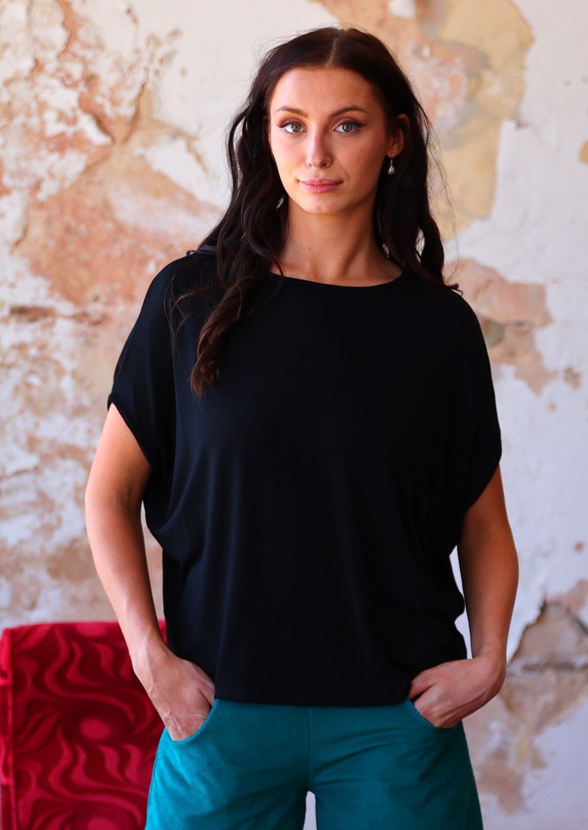 Woman wearing batwing t-shirt black over teal corduroy pants 