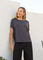 Woman wearing a dark grey short sleeve batwing top with a round neckline, paired with black pants
