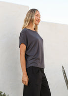 Woman wearing a dark grey relaxed fit stretch rayon t-shirt and black pants against a white wall.