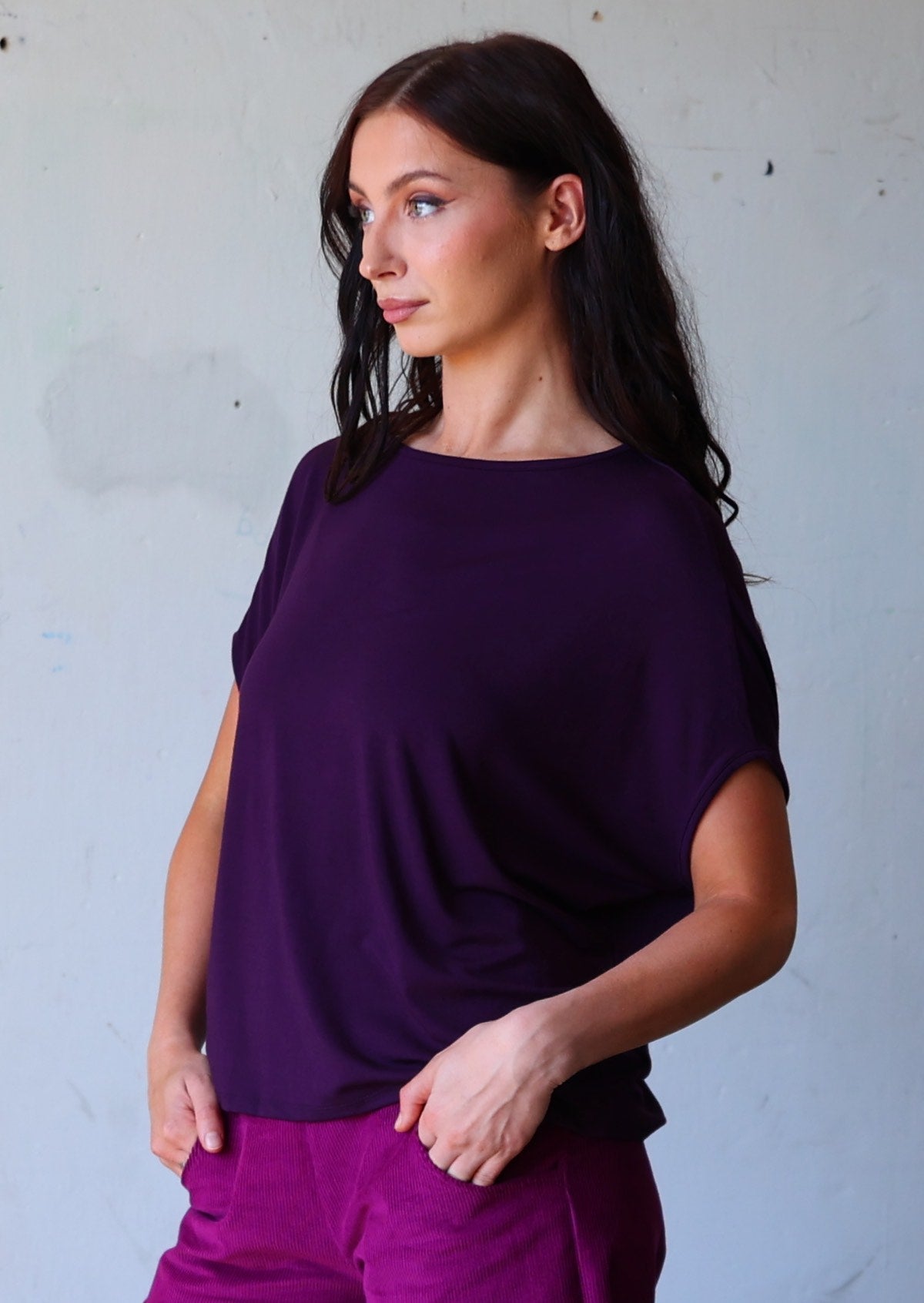 woman with dark hair wearing purple batwing t-shirt and purple corduroy pants