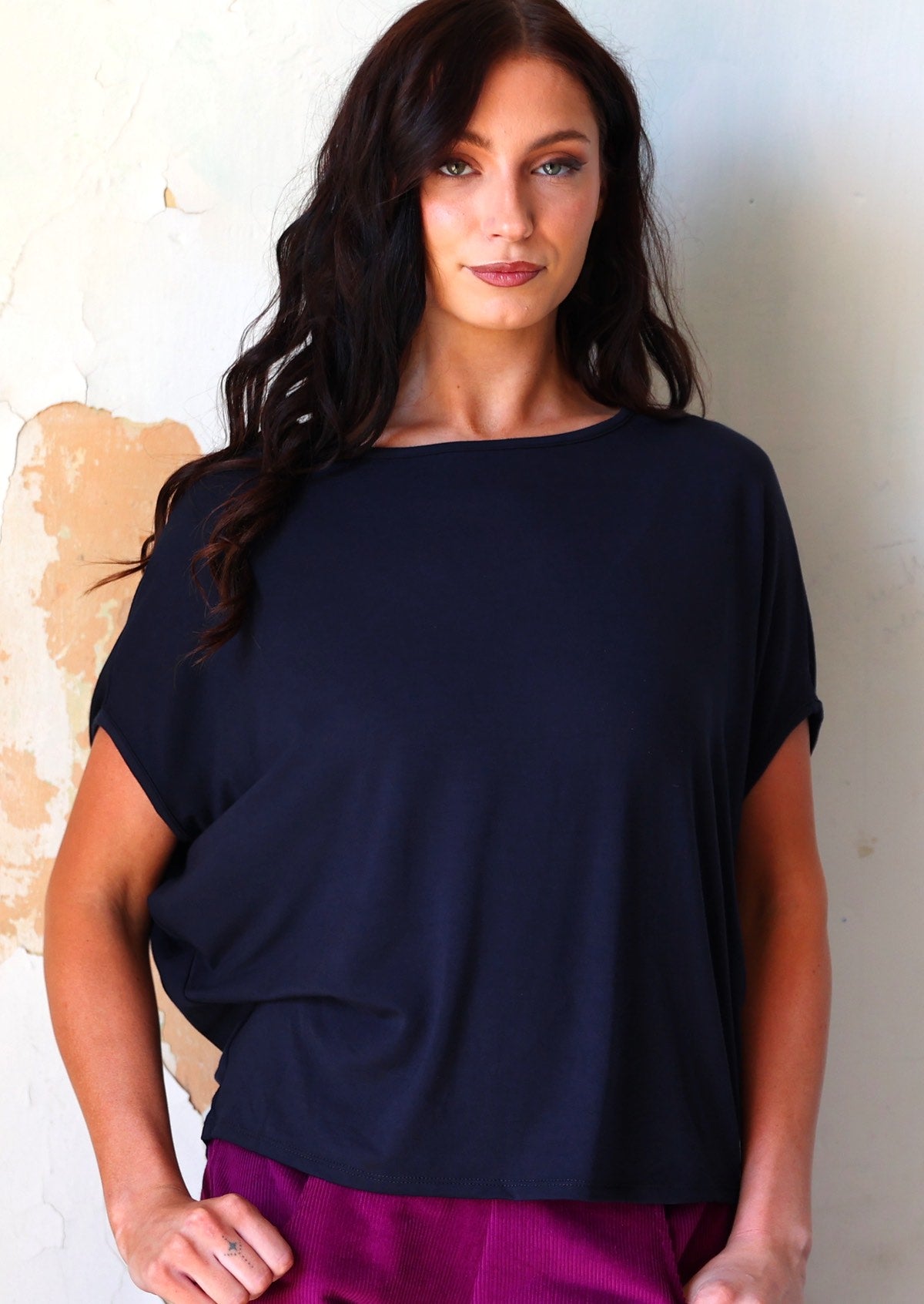 Woman wearing navy blue rayon batwing t-shirt over purple corduroy pants