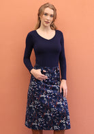 Woman wearing A-line, midlength corduroy skirt with printed florals on navy blue base.
