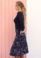 Side pose of model wearing a beautiful floral printed cord skirt with side zip and one hand in back pocket.
