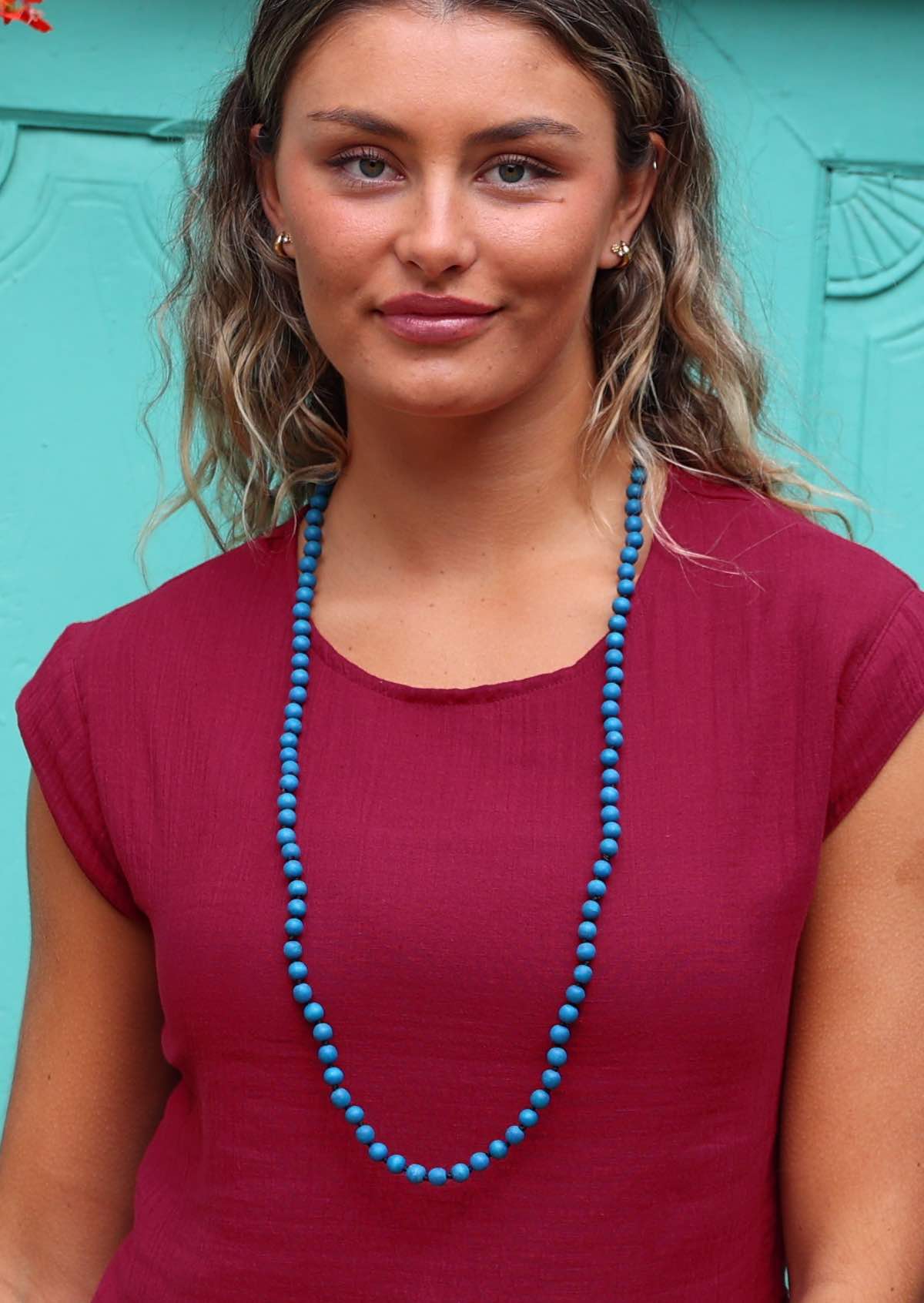 woman wearing blue wooden beads over red cotton top