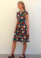 Model standing to the side wearing 100 percent cotton dark navy blue base and bright abstract floral print cotton retro dress and heeled sandals 