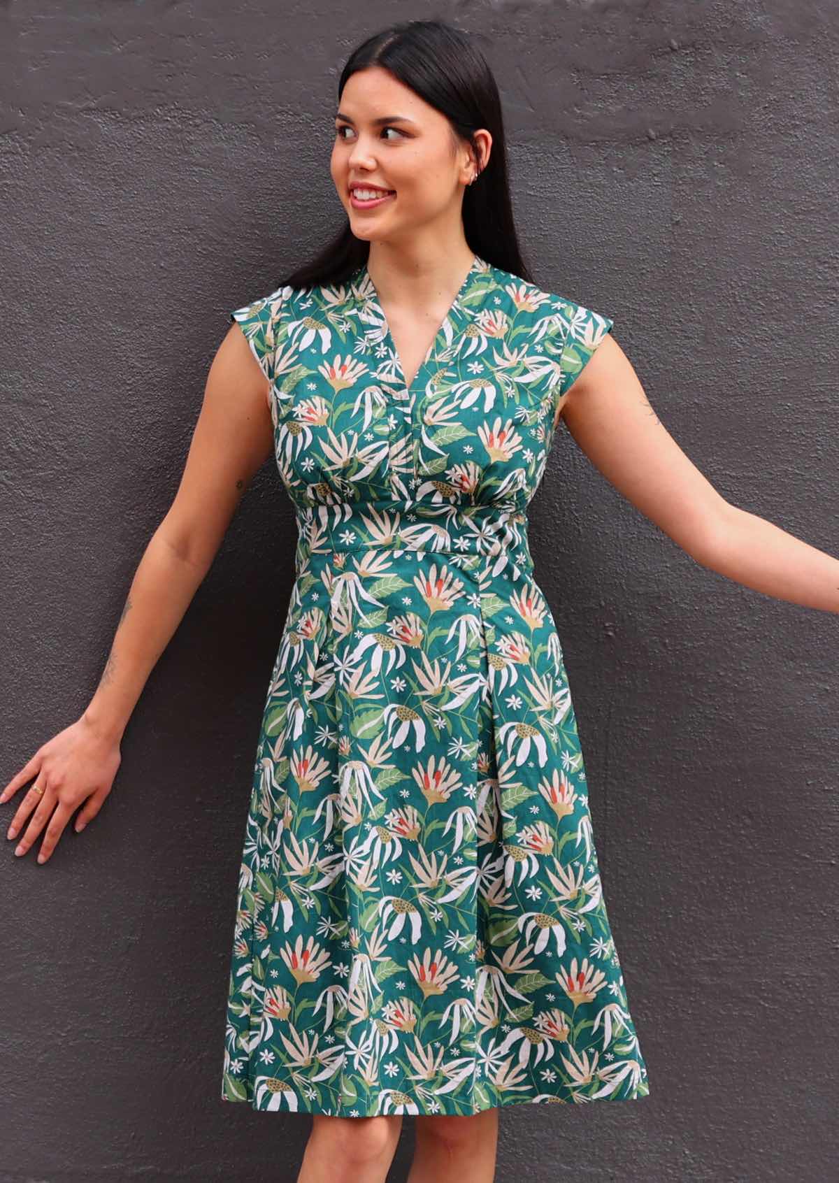 Model posing in front of wall wearing floral dress with dark green background 100 percent cotton retro style 