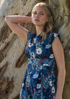 Close up of model leaning on tree in cotton blue floral dress with fitted waistband with two box pleats underneath