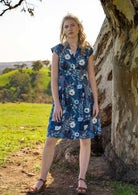 Model poses in knee length cotton blue floral dress with fitted bodice and box pleats at waist to give A-line skirt