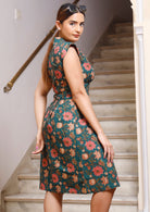 Side pose of model in pinkish bold floral printed, retro style dress with cap sleeves and fitted waist 
