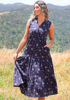 Woman holds skirt of cotton sleeveless maxi dress with buttoned bodice with her hand in side pocket