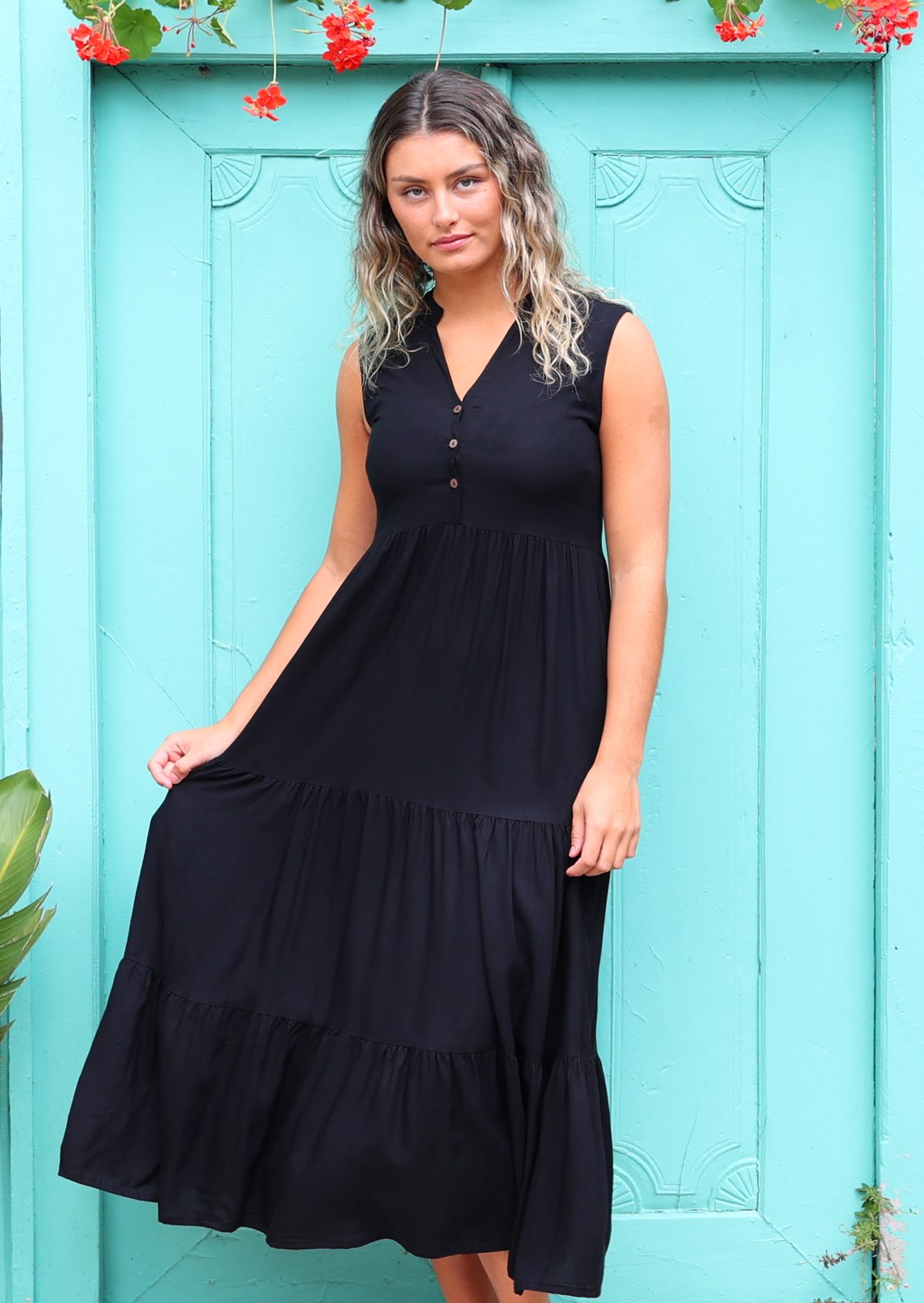 Woman wearing long black casual dress with buttons up front in front of aqua door