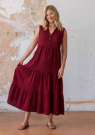 Woman poses in deep red double cotton sleeveless maxi dress with flowy skirt