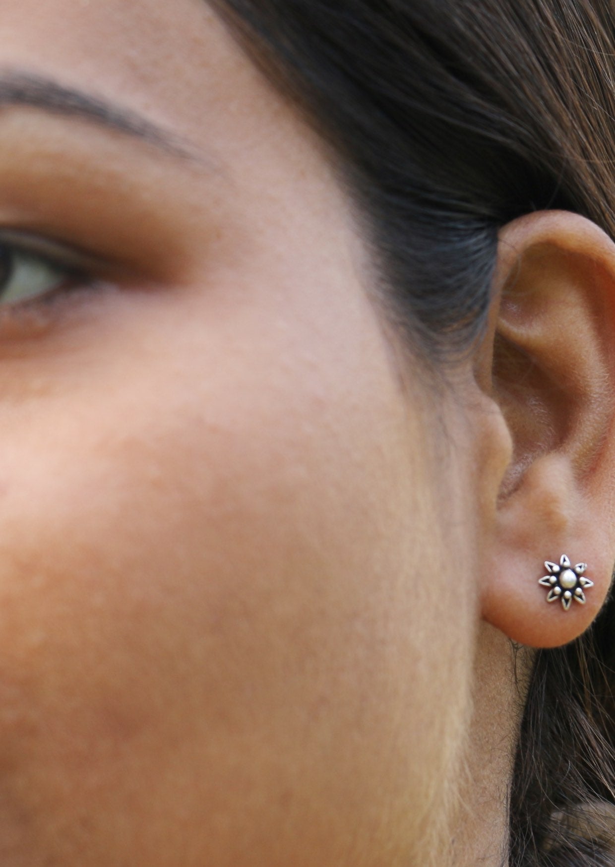 Close up of a person wearing a floral stud earrings with delicate floral design 