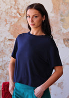 woman in navy blue rayon loose fit t-shirt  over teal corduroy pants with hands in pockets 